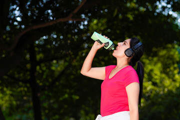 Indian woman drinks water from a bottle after running in the park.