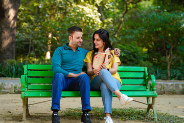 Young indian man and woman reading book at park.