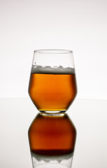 Vertical closeup of glass of foamy whiskey on a white background with a reflection