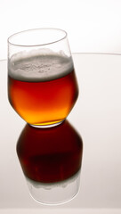 Vertical closeup of glass of foamy whiskey on a white background with a reflection