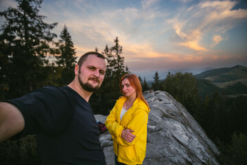 Couple hikers taking a selfie on top of a mountain, summer sunset time. Man and woman looking at beautiful inspirational landscape view, copy space