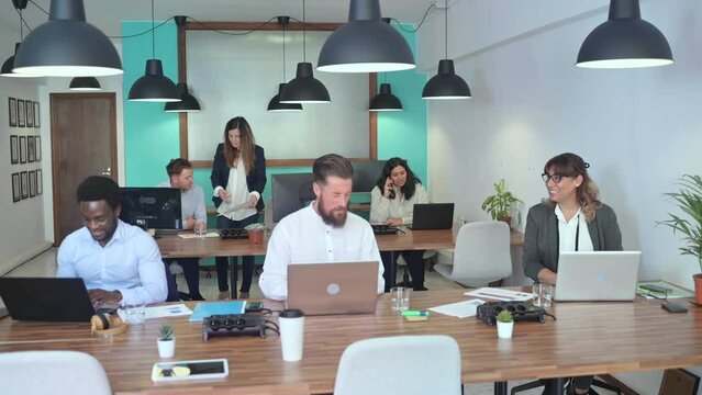 Real time high angle of multiracial colleagues in formal outfits sitting in open space office at tables with laptops while communicating and discussing details of business project