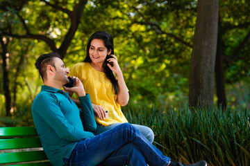 Young man sitting at park with young woman at talking on smartphone