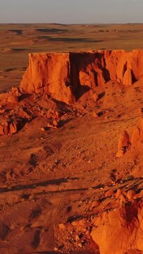 Aerial around view of the Bayanzag flaming cliffs at sunset in Mongolia, found in the Gobi Desert. Vertical video