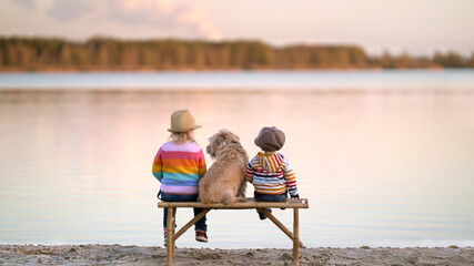 zwei Kinder mit Hund auf einer Bank am See