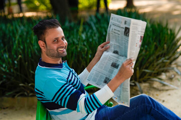 Young indian man reading news paper at park.