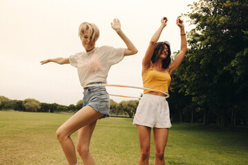 Mature female friends enjoy playing with a hula hoop in a park