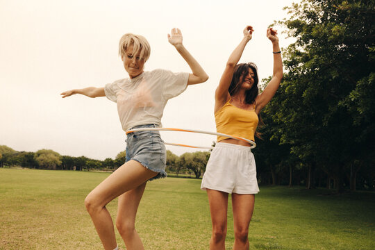 Mature female friends enjoy playing with a hula hoop in a park