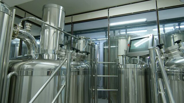 Arc shot of shiny stainless steel brewhouse with large mash tun, lauter tun and brewkettle, stairs, work platform and operating post with touchscreen control panel