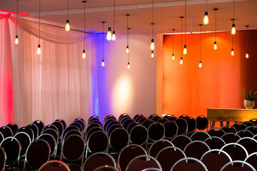 Empty chairs in the hall illuminated by hanging lamps against the colorful walls.