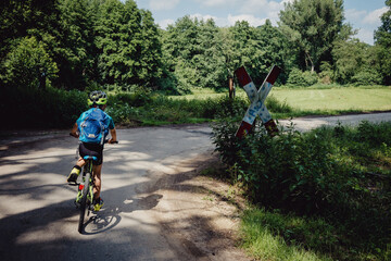 Junge passiert das Ortsschild einen Bahnübergang während einer Fahrradtour durch das Münsterland in den Sommerferien, Deutschland