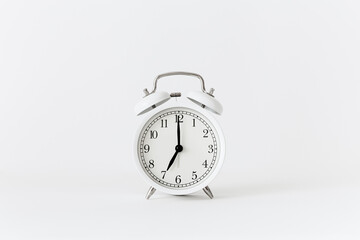 Classic white alarm clock on a white background. Alarm clock show 7 O'Clock with copy space.