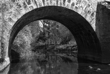 View through arch of Roman bridge on old royal road from Paris to Sens over Yerres river near Brie-Comte-Robert. Built in 17th-18th c. recalls architects name, Romains brothers. Black white photo - obrazy, fototapety, plakaty