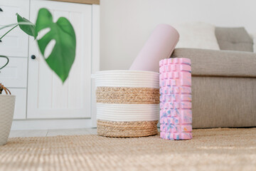 A pink foam massage roller and yoga mat at floor in living room. Foam rolling is a self myofascial...
