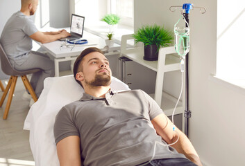 Male patient undergoing intravenous vitamin therapy course treatment. Relaxed young man getting IV line medicine infusion while lying on bed at clinic or medical office