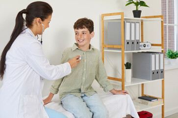 Child patient getting health checkup at doctor's office. Pediatrician uses stethoscope to examine heart or lungs of happy little school boy sitting on medical couch in exam room at pediatric clinic