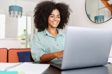 Fototapeta na wymiar Successful female freelancer. Happy millennial woman sitting at desk with laptop, smiling and typing, enjoying remote work, female student studying on the distance