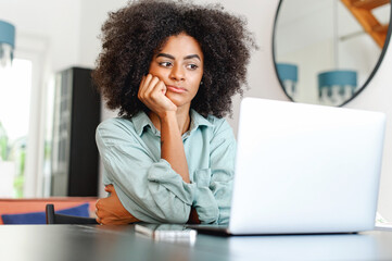 Obraz premium Bored woman feels lack of motivation, remote employee feeling weary because lacks interest in current activity, sitting in front of laptop, resting chin with hand in home office