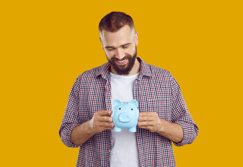 Adult bearded man with blue piggy bank on yellow background. Concept of saving money or investment....