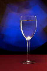 Vertical closeup of water in a wine glass against a blue neon light in a studio