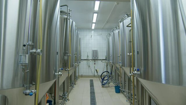 Dollying shot of rows of numbered stainless steel beer fermenting tanks with gauges and sample taps in operation at medium-sized independent craft brewery