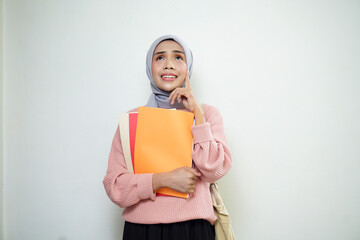 Smiling Asian Muslim female student in pink sweater with medium bag, holding book and thinking isolated on white background. back to school concept