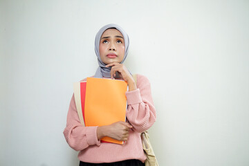 Smiling Asian Muslim female student in pink sweater with medium bag, holding book and thinking isolated on white background. back to school concept