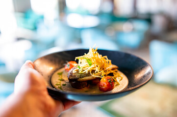 man hand hold Fried fillet dorado fish with tomatoes, lemon and sauce on plate