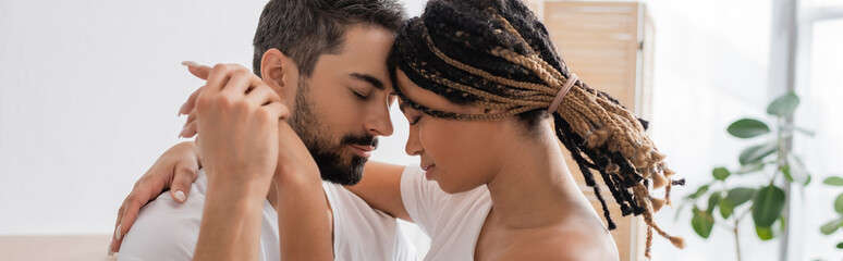 side view of bearded man and young african american woman with dreadlocks embracing and holding hands, banner.