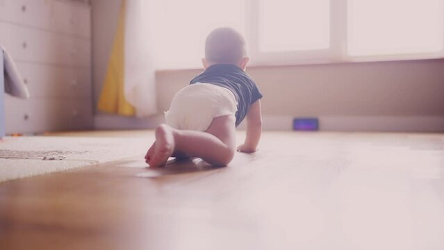 baby learns to crawl on the floor at home. happy family kindergarten kids concept. First steps, baby crawling view from the back. baby learns to crawl to explore the world around dream him