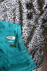 Leopard print shirt, pleated green skirt, retro sunglasses, pearl barrettes and brass rings. Top view.