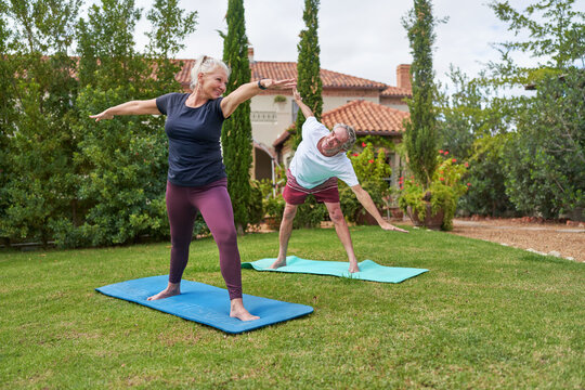 Happy, active senior couple practicing yoga in villa garden