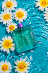 Vertical shot of a perfume bottle on water with daisies against a blue background with copy space