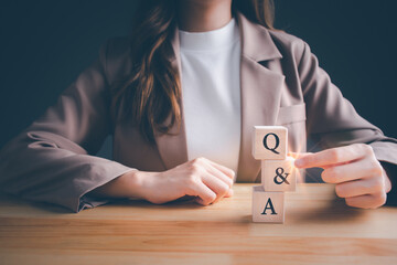 Businesswoman holding Q and A, text with wooden cube block on the table. FAQ (frequency asked questions), Answer, Question Ask, Information, Communication, Brainstorming and Business Concepts. - obrazy, fototapety, plakaty