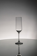 Grayscale shot of an empty glass cup with reflection on a mirror surface