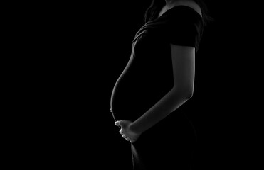 Silhouette of a pregnant woman wearing a black dress, black background