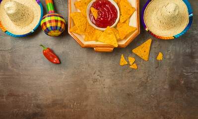Mexican party table with nacho chips, maracas and sombrero hat on dark background. Cinco de Mayo holiday celebration. Top view, flat lay