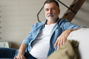 Happy mature man sitting on couch. Portrait of man relaxing at home with big smile.