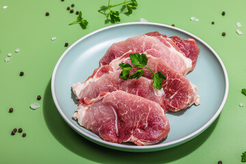 Pieces of pork meat with parsley on gray dish, raw fresh steaks concept. Sea salt, spices