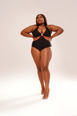 Woman posing on light gray studio background, wearing black fashionable swimwear. Body positive, conscious concept. Afro hairstyle.