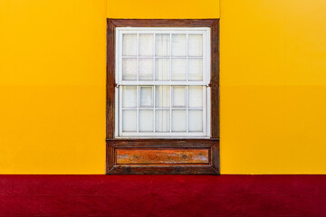 Ventana de madera en fachada amarillo y rojo de estilo colonial 