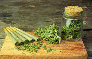 Pre-Roll cannabis joints are placed on the wooden chopping board with cannabis buds in a clear...