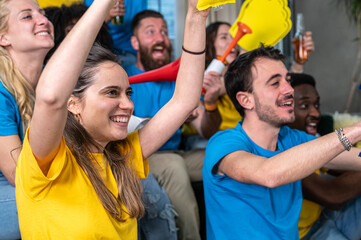 Friends watching sports thrones on television and rejoicing in victory while sitting on the ground or on the sofa, focus on brunette young girl