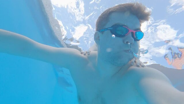 a man wearing swimming goggles dives in the pool and takes a picture of himself.