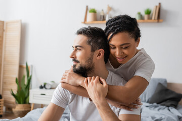Fototapeta premium happy african american woman embracing dreamy bearded man looking away in bedroom at home.