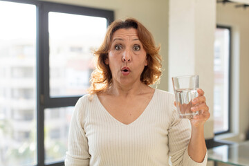 middle age pretty woman feeling extremely shocked and surprised. water glass