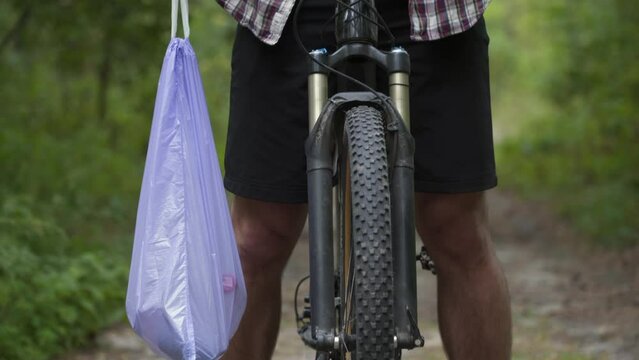 Man riding bicycle through forest, picking up trash. Trendy sports plogging programs to help save nature. Pollution of environment. Ecological issue. Plastic ban awareness, national cleanup days idea