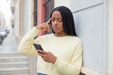 black afro woman looking surprised, realizing a new thought, idea or concept. using a smartphone...