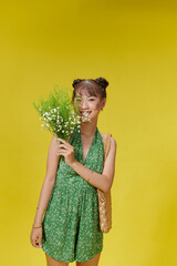 Charming asian woman in green summer jumpsuit with wildflowers in her hands smiling