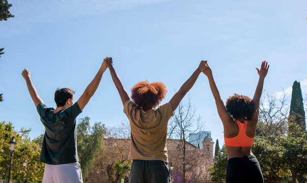 Joyful diverse friends raising arms in park
